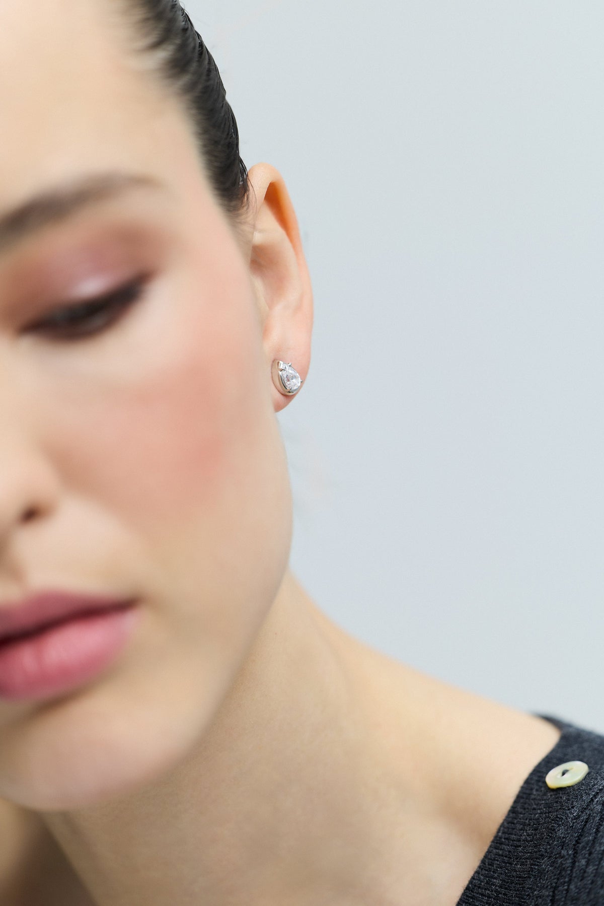 HALF OF A MODEL’S FACE IN FRAME WITH THE FOCUS ON HER EAR, AS SHE WEARS THE PEAR STUD FROM THE DELANCEY STUD SET OF EARRINGS