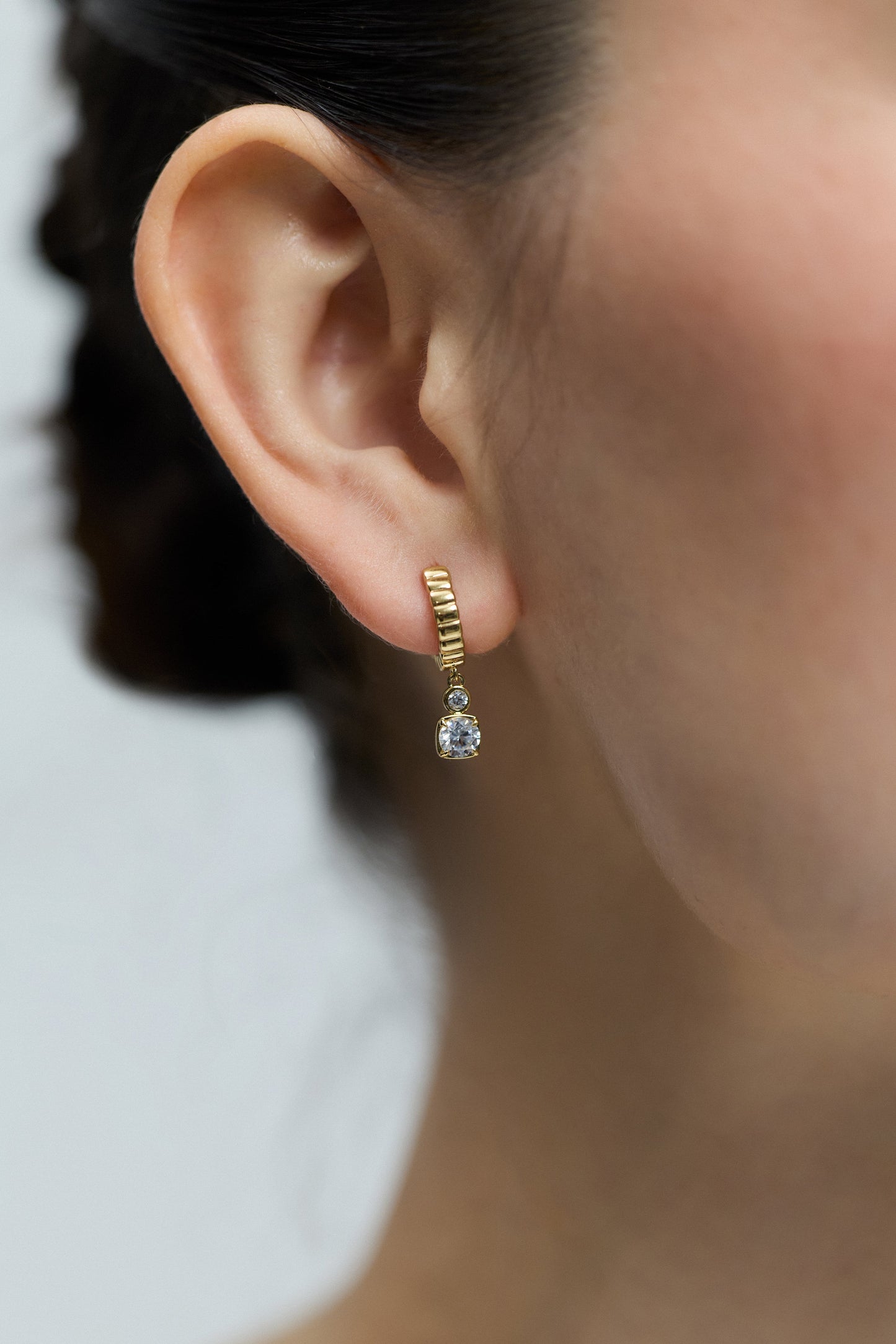 CLOSE UP OF A MODEL’S EAR, WEARING THE DELANCEY SMALL CHARM HOOP EARRINGS IN GOLD PLATING