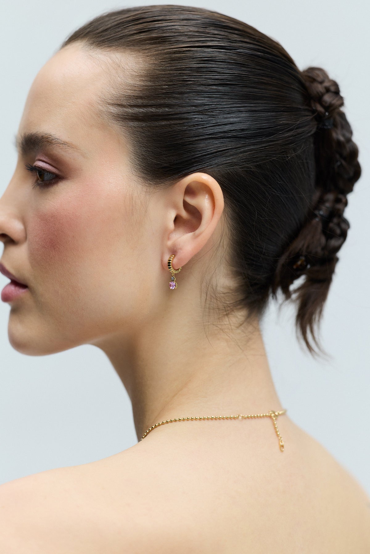 SIDE PROFILE OF A MODEL WITH A TWISTED BRAID UPDO IN HER HAIR, AND THE DELANCEY PINK SMALL CHARM HOOP EARRINGS IN HER EAR