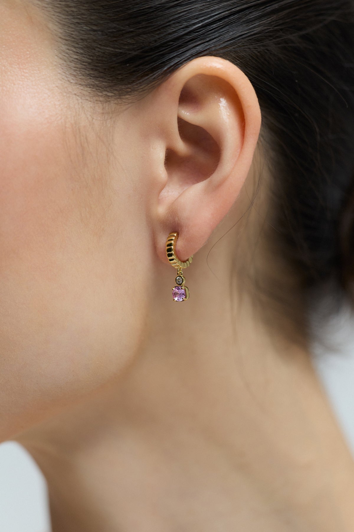 CLOSE UP OF A MODEL’S EAR WEARING THE DELANCEY PINK SMALL CHARM HOOP EARRINGS