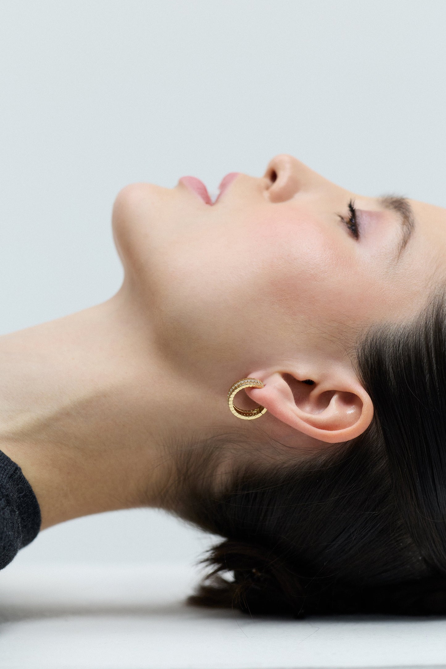 SIDE PROFILE OF A MODEL LAYING DOWN, WITH HER HAIR IN AN UPDO UNDER HER AND THE DELANCEY PAVE STRIPE HOOP EARRINGS IN HER EARS