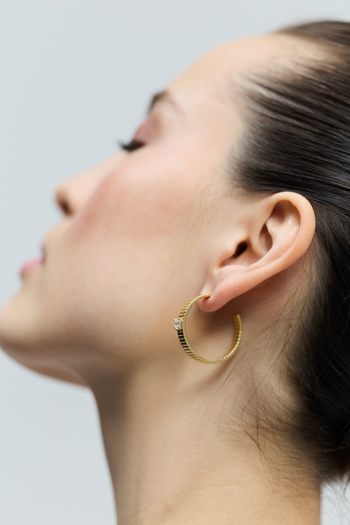 CLOSE-UP OF THE BACK OF A MODEL'S HEAD AS SHE TURNS SLIGHTLY TO THE SIDE, WITH HER EAR IN FOCUS WEARING THE DELANCEY LARGE C HOOP EARRINGS.