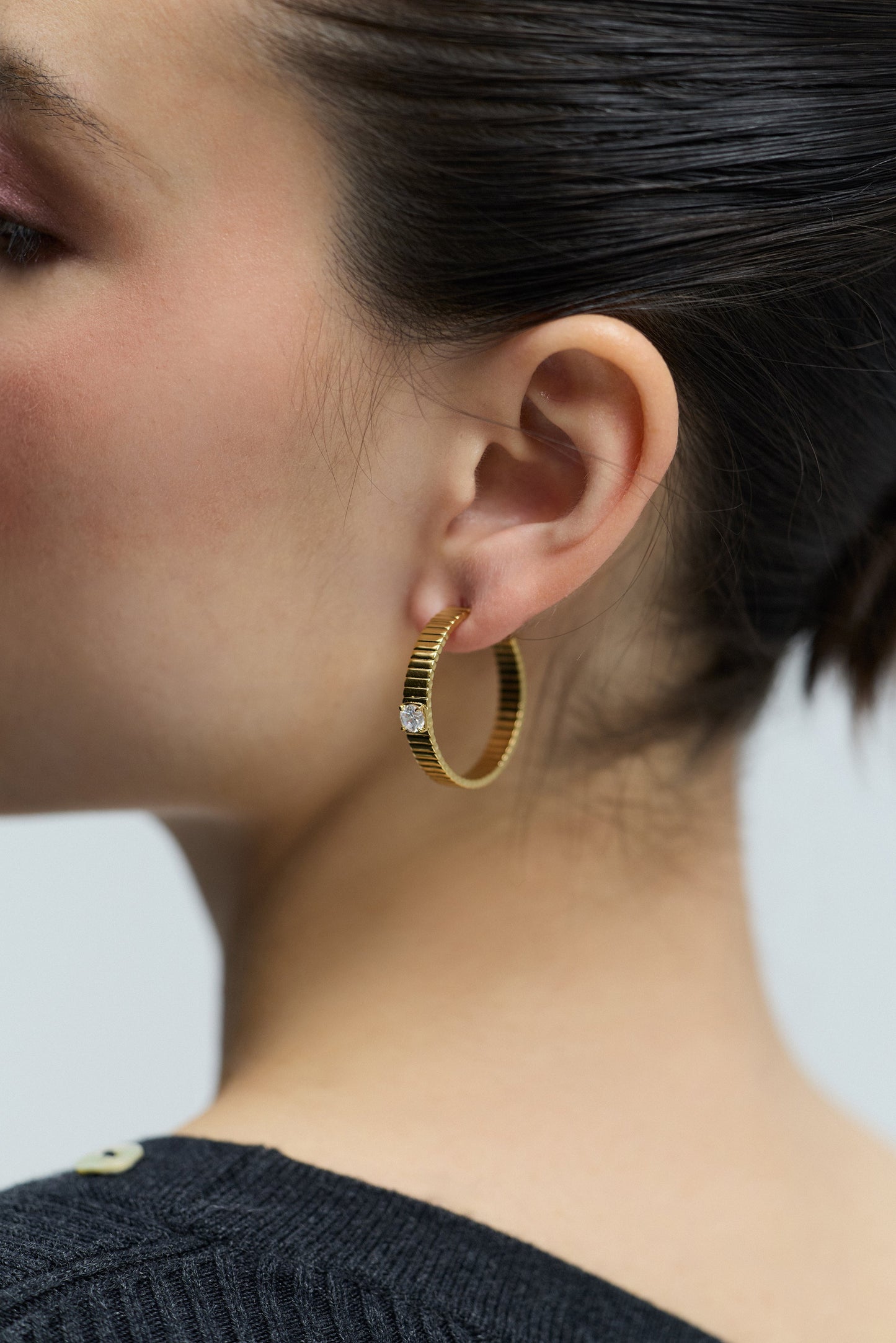 CLOSE UP OF A MODEL’S EAR AS SHE TURNS TO THE SIDE, WEARING THE DELANCEY LARGE C HOOP EARRINGS
