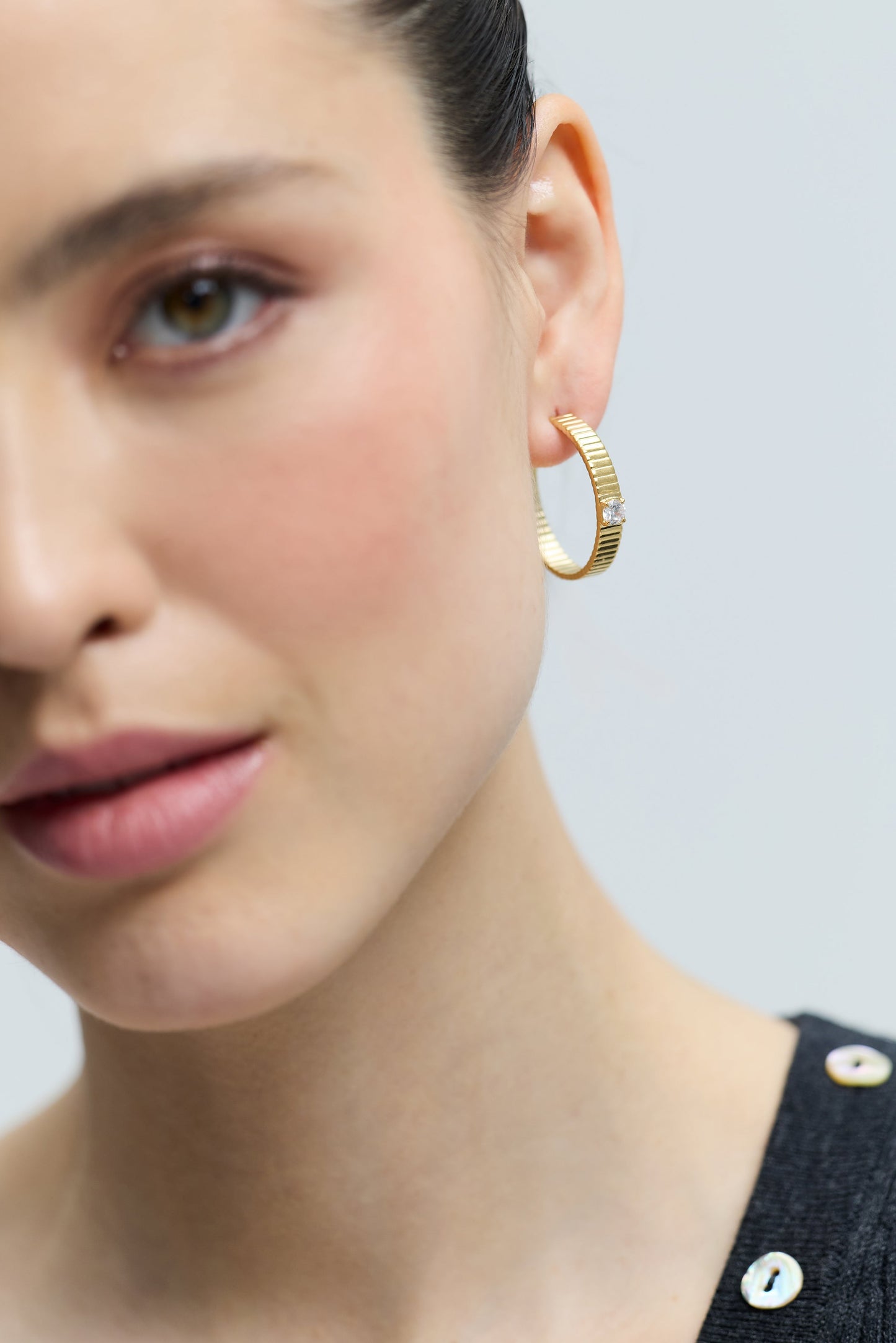 CLOSE UP OF HALF OF A MODEL’S FACE WITH JUST HER EAR IN FOCUS, AS SHE WEARS THE DELANCEY LARGE C HOOP EARRINGS