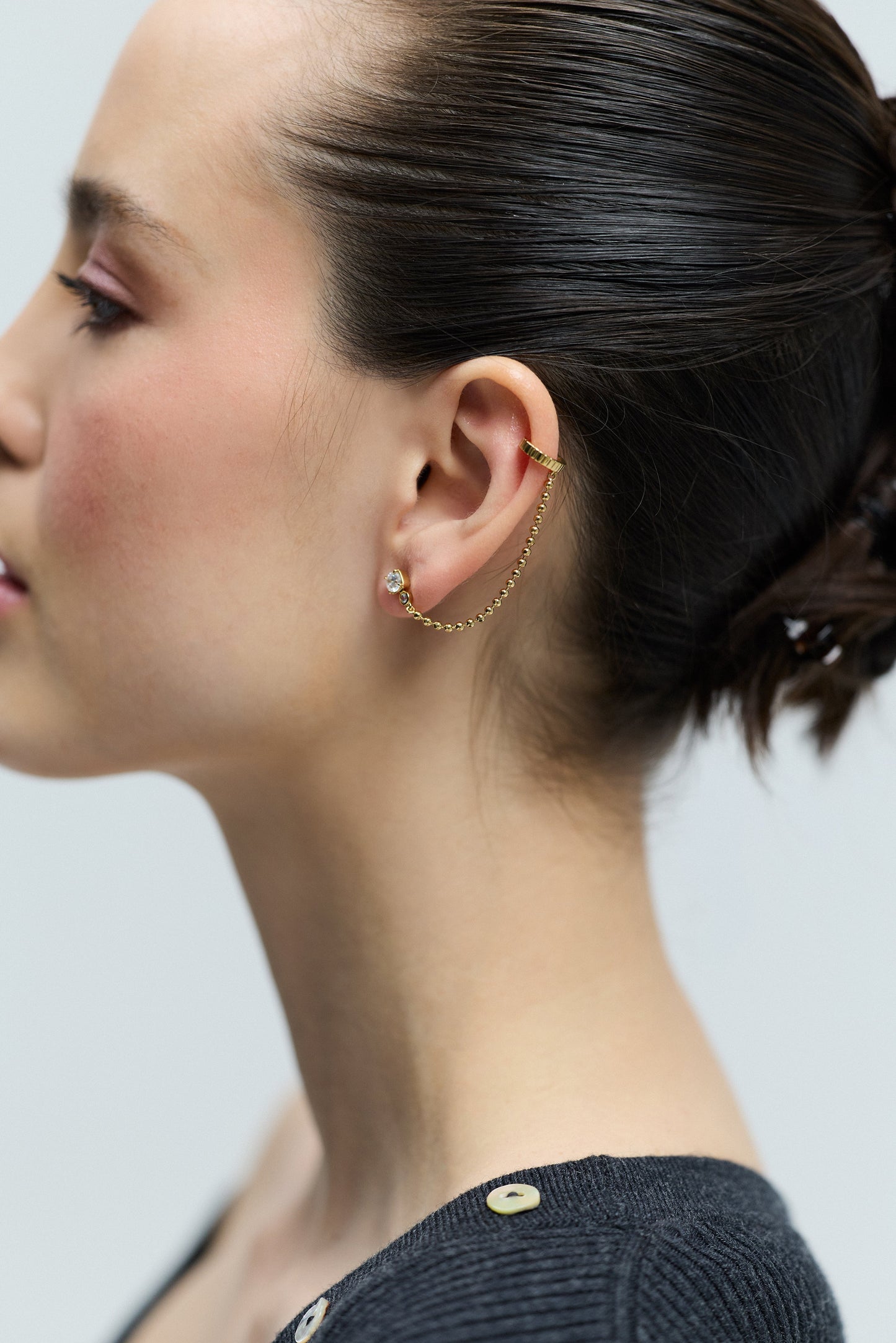 SIDE PROFILE OF A MODEL WITH AN UPDO HAIRSTYLE WEARING A GRAY SWEATER AND THE DELANCEY SINGLE SWAG CUFF EARRINGS
