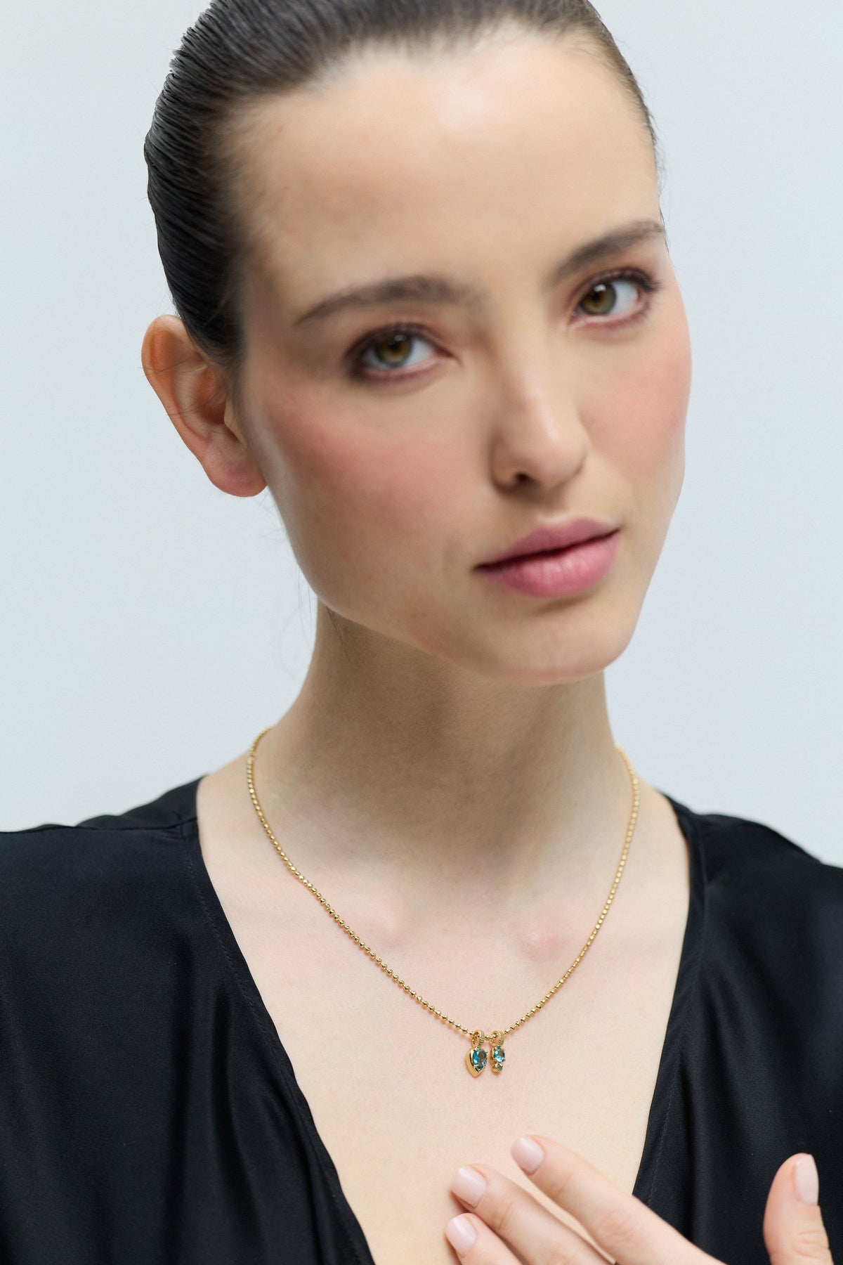 A MODEL LOOKING AT THE CAMERA WEARING A BLACK TOP AND THE DELANCEY AQUA CHARM PENDANT NECKLACE