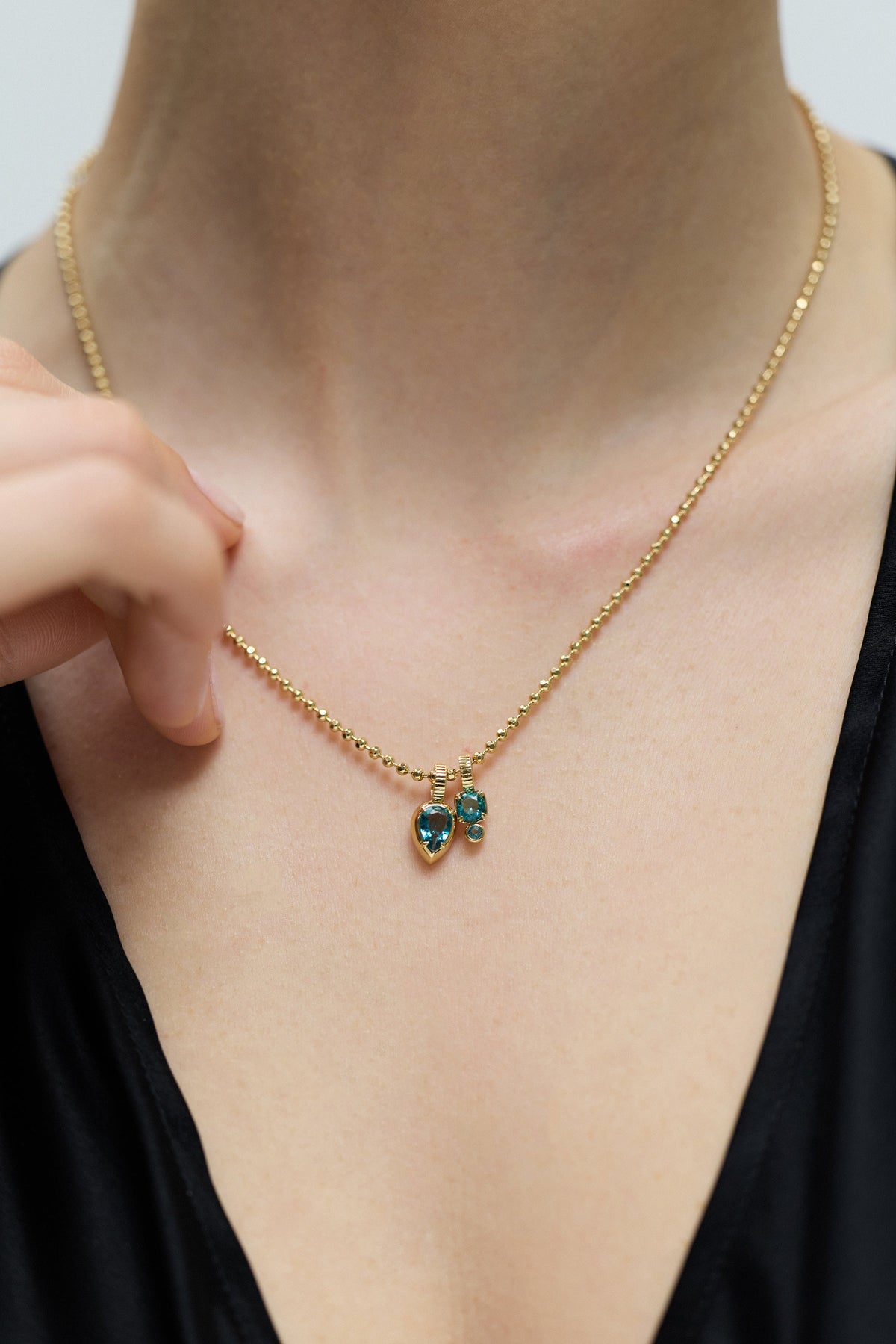 CLOSE UP OF A MODEL’S CHEST WEARING A BLACK TOP AND THE DELANCEY AQUA CHARM PENDANT NECKLACE
