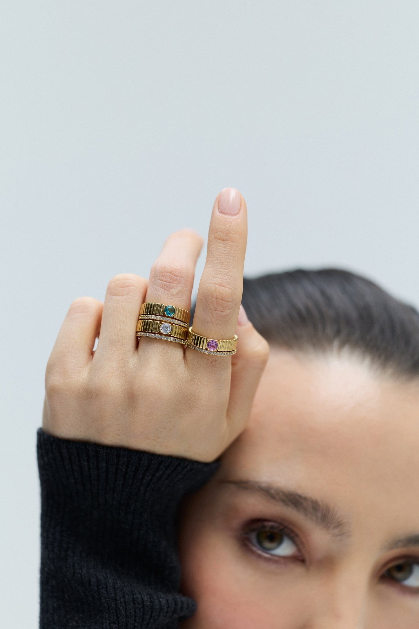CLOSE UP OF A MODEL FROM THE EYES UP, WITH HER HAND RAISED BESIDE HER FACE AND IN FOCUS, WEARING DELANCEY SOLITAIRE RING SETS ON HER FINGERS