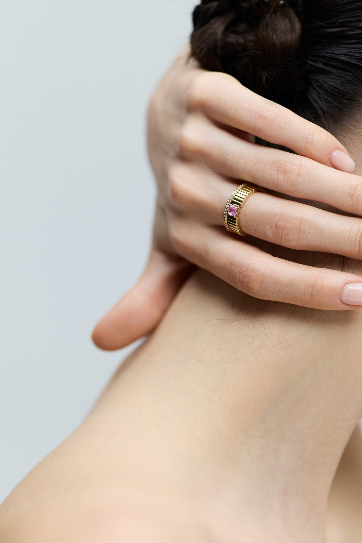VIEW OF THE BACK OF A MODEL’S NECK AS SHE TURNS TO THE SIDE, WITH HER HAND RESTING ON THE BACK OF HER NECK, WEARING THE DELANCEY PINK SOLITAIRE RING