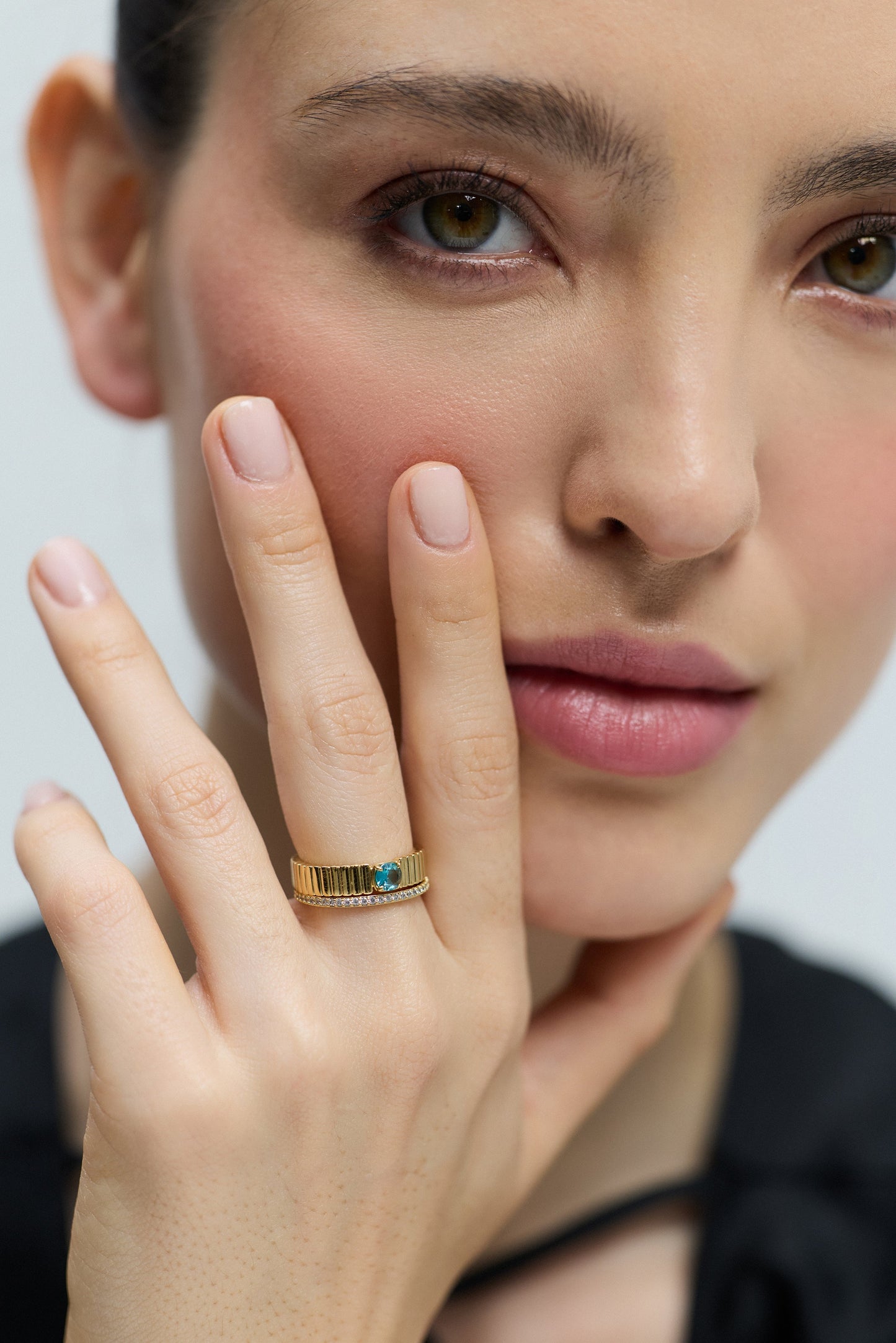 CLOSE UP OF A MODEL LOOKING AT THE CAMERA WITH HER FINGERS LIFTED UP TO HER FACE, WEARING THE DELANCEY AQUA SOLITAIRE RING