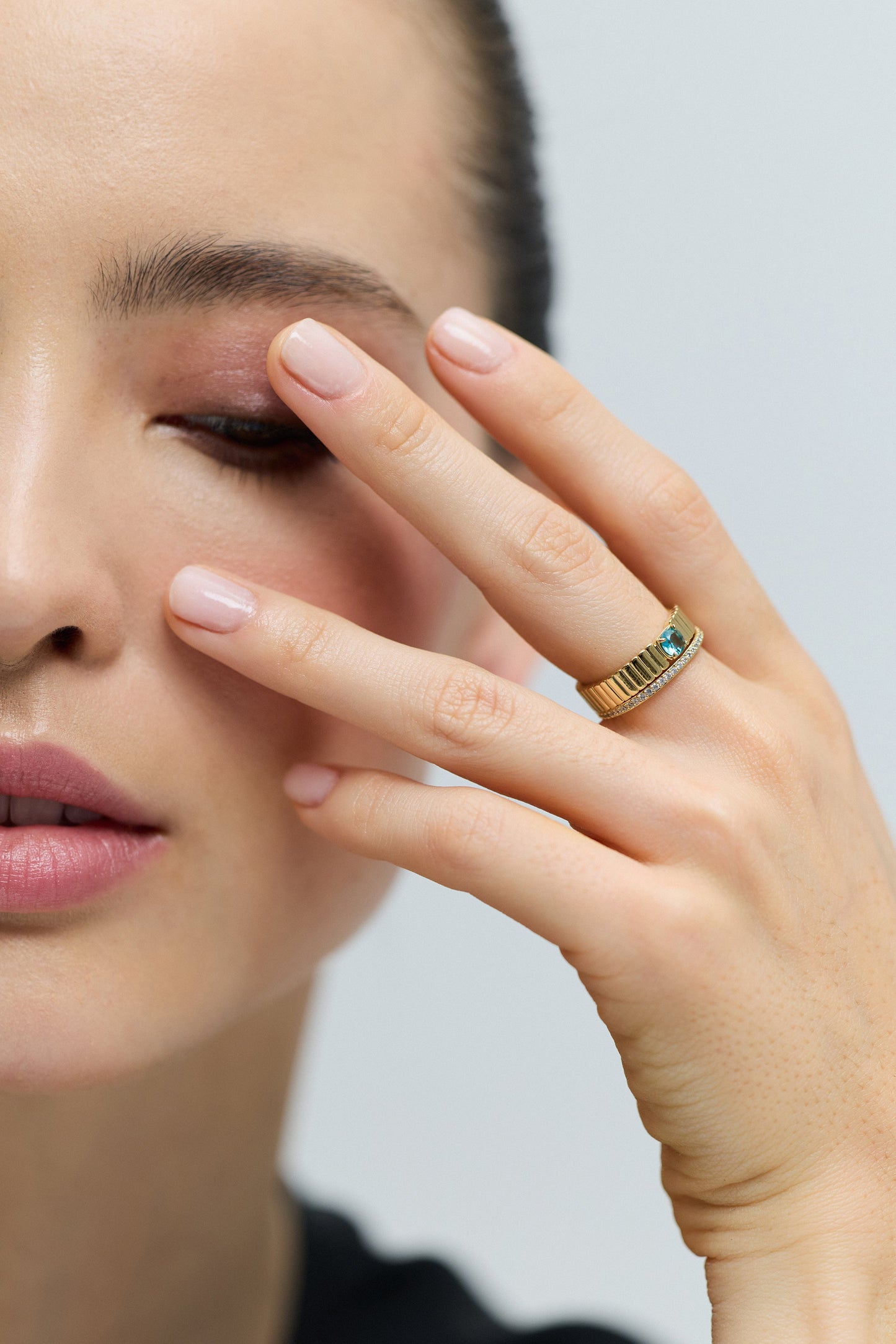 HALF OF A MODEL’S FACE IN FRAME WITH HER FINGERS LIFTED UP TO HER EYELIDS, WEARING THE DELANCEY AQUA SOLITAIRE RING