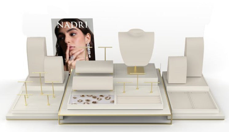 A jewelry display stand set in a clean studio setup, featuring cream-colored display blocks, gold-tone jewelry stands, and a central display tray. A graphic insert with the brand name 'NADRI' is visible behind the display.