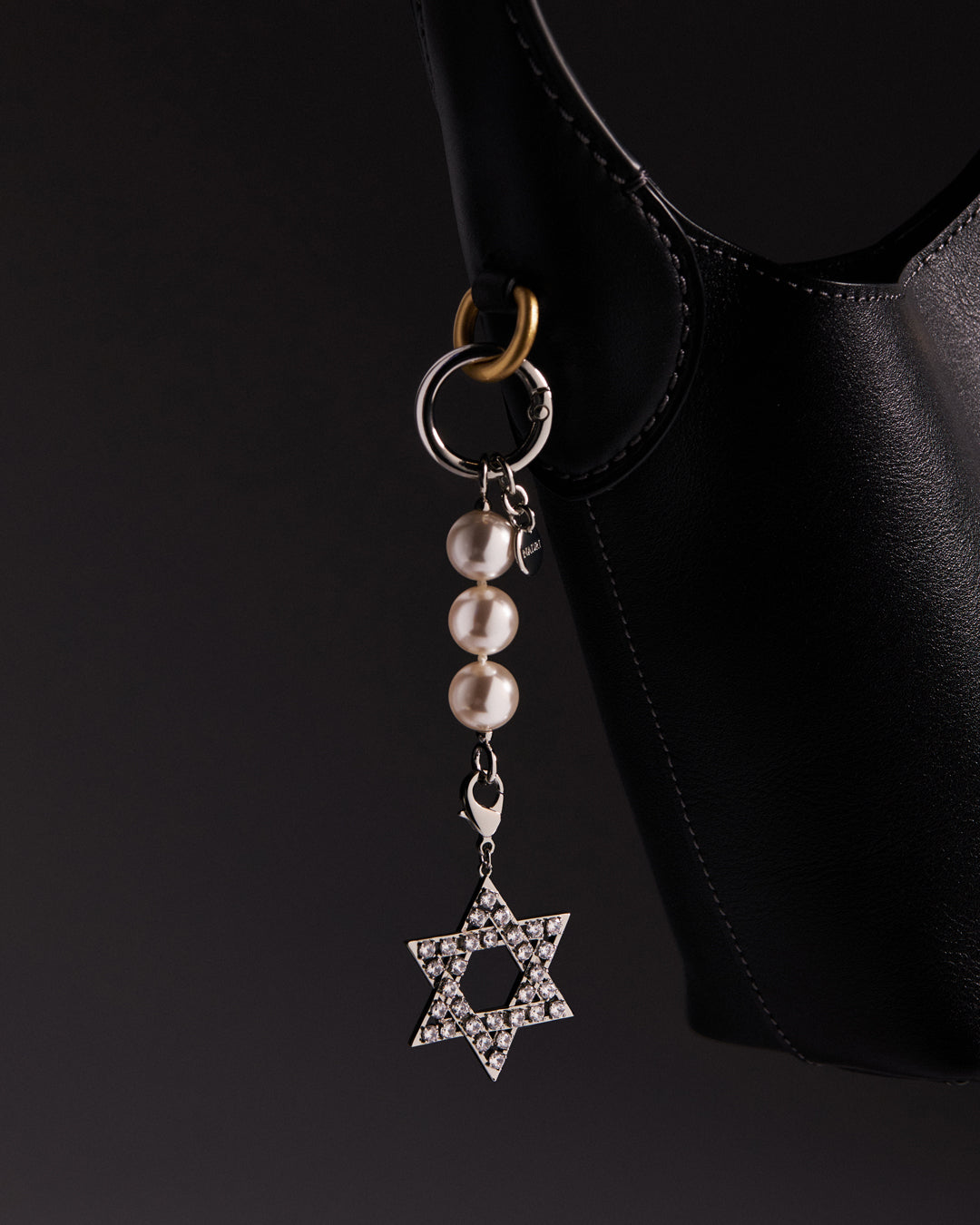 Star of David bag charm with a pearls chain on a black handbag against a dark background.