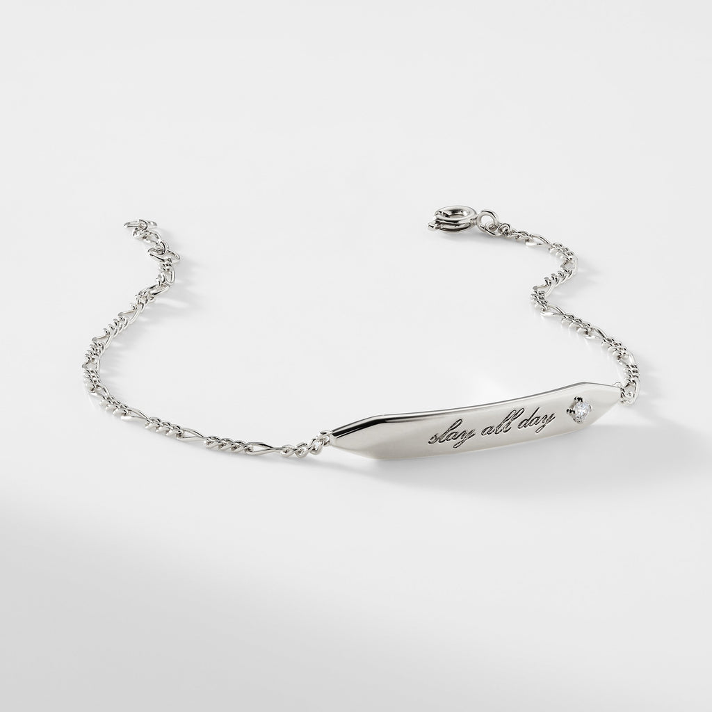 A silver ID bracelet that says "slay all day" with a cubic zirconia stone