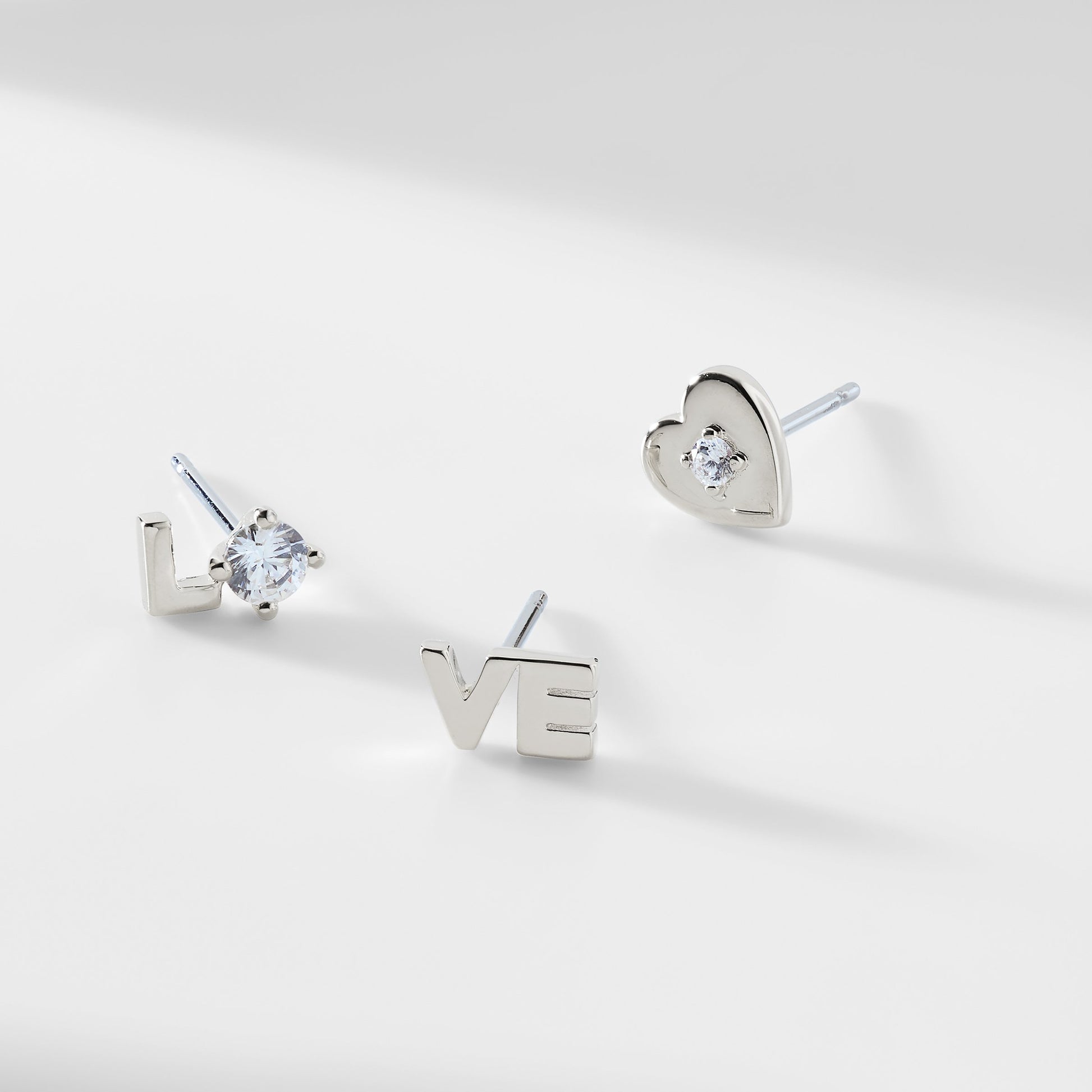 Silver stud earrings that spell out "LO-VE" and a silver heart stud earring with a CZ stone