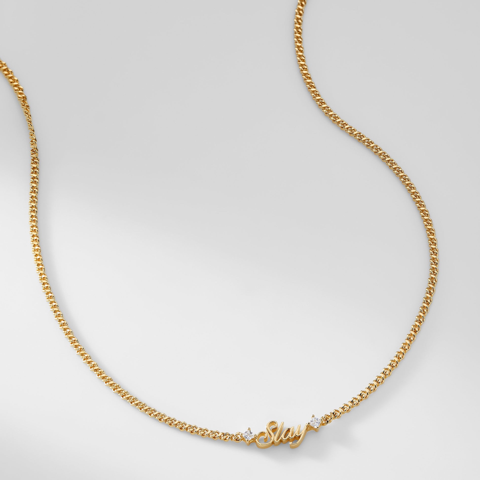 A gold chain necklace that says "Slay" with two cubic zirconia stones